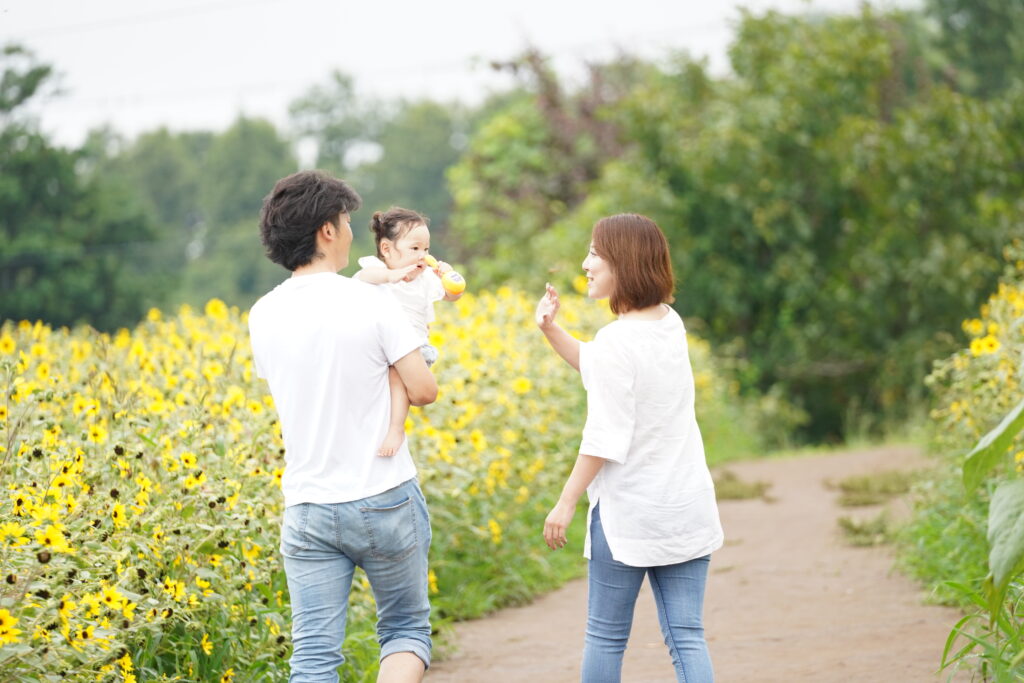 お散歩フォト撮影で赤ちゃんを抱いた家族が花畑の中を歩いている様子
