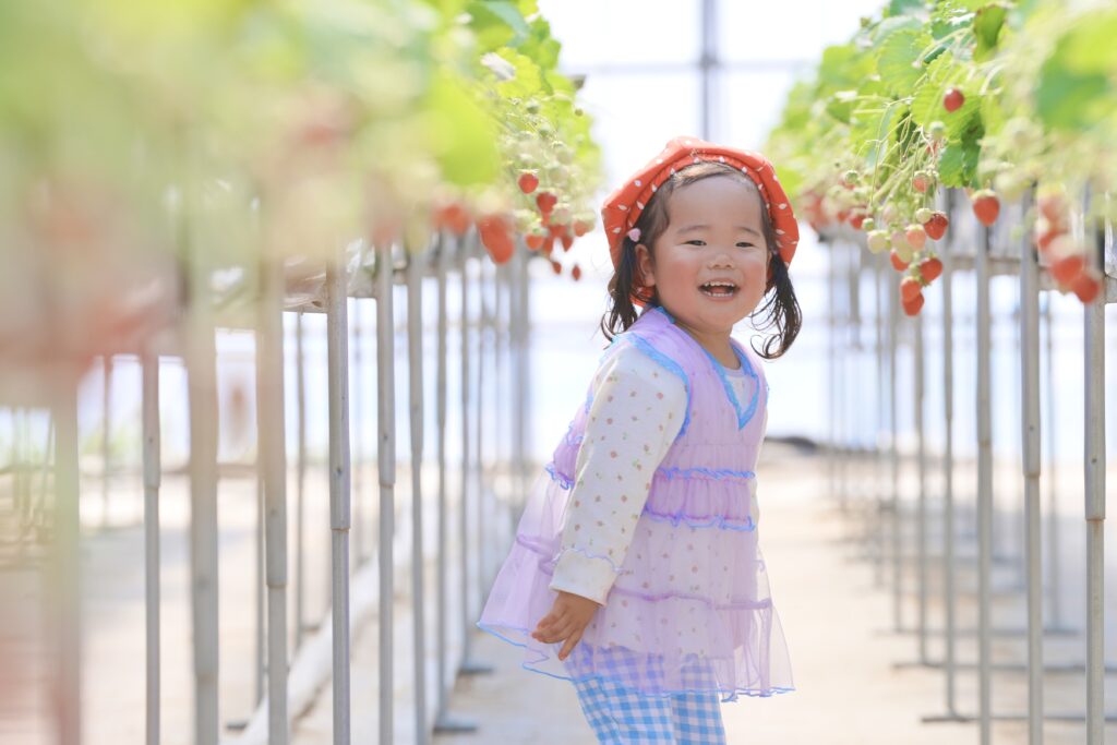 いちご狩り撮影会でいちご農園に立つ女の子が笑顔を見せている様子